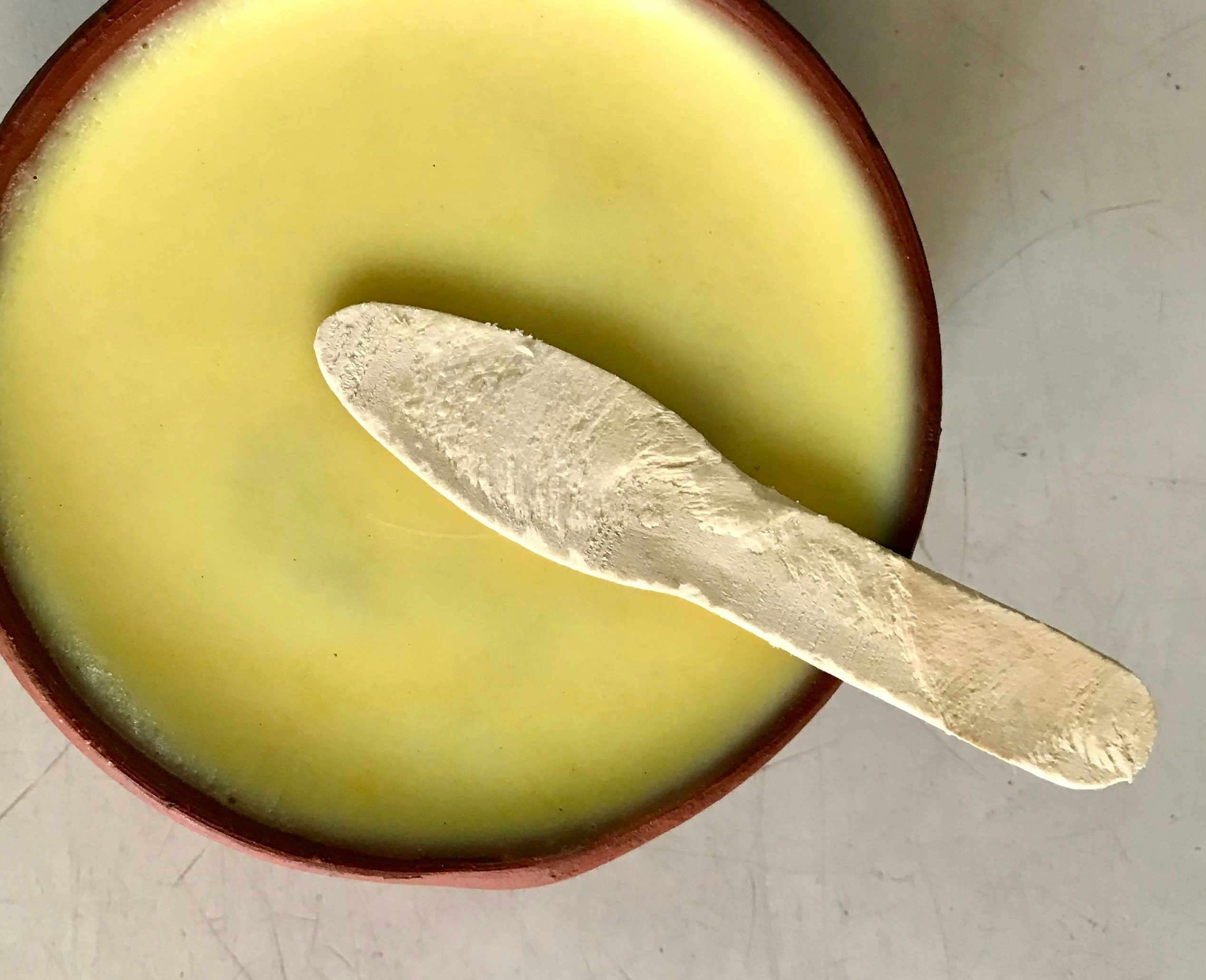 Natural cocoa butter in a bowl with a wooden spatula sitting above it.